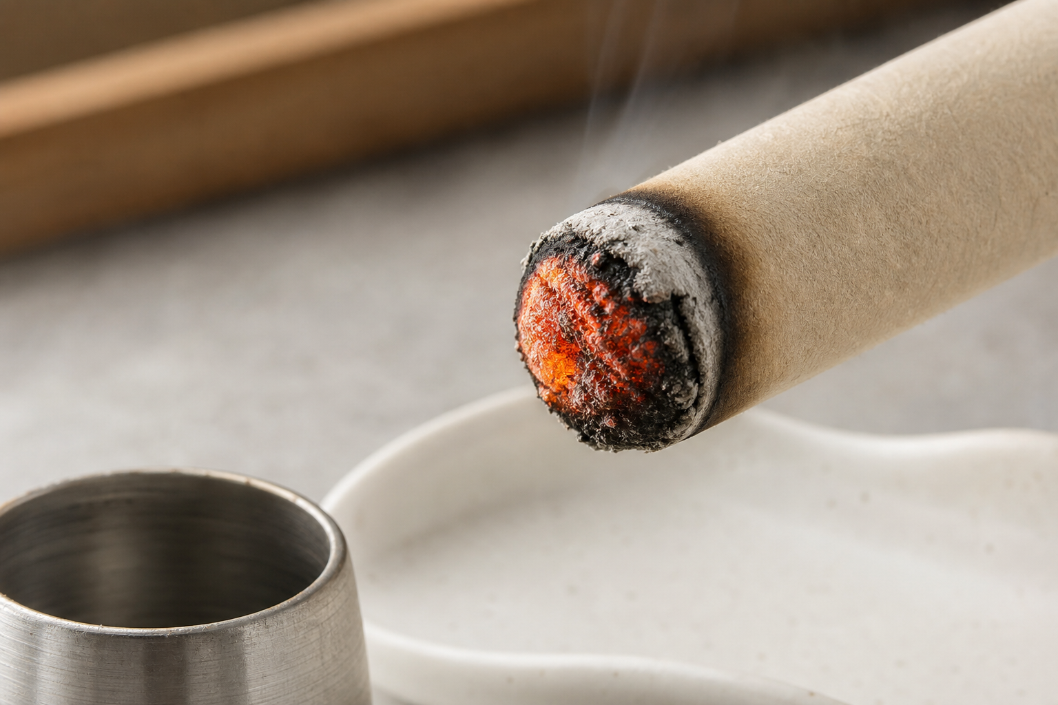 Close-up of a moxa stick tip glowing evenly with a ring of ash above a tray and metal snuffer cup.